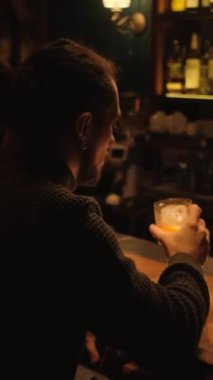 Bir gece barında genç bir adamın portresi. Bir adam kokteyl içer ve dinlenir. Dikey video.