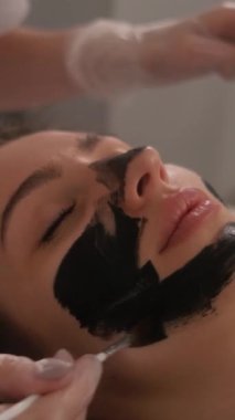 Genç ve güzel bir kızın yüzünün karbonu soyuluyor. Cilt bakımı kozmetolojisi. Lazer terapisi ve cilt tedavisi. Dikey video.