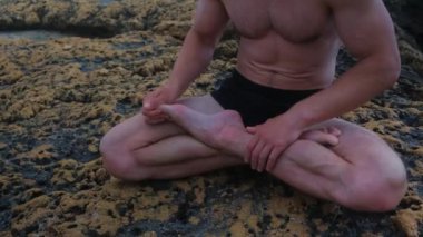 Deniz kıyısındaki bir adam yoga yapar ve lotus pozisyonunda oturur..