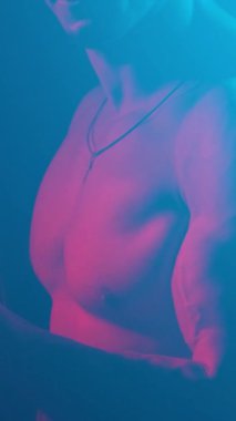 Young muscular guy in the studio with new lights and smoke. Vertical video.