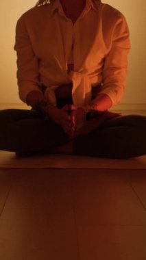 A woman sits in a lotus position in the twilight with candles burning on the rug. Yoga practice and total relaxation. Vertical video.