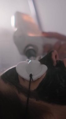 Genç ve güzel bir kızın yüzünün karbonu soyuluyor. Cilt bakımı kozmetolojisi. Lazer terapisi ve cilt tedavisi. Dikey video.