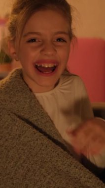 Akşamları odada oturup televizyon izleyen ve gülen bir çocuğun portresi. Kız komik bir film izliyor ve mutlu. Dikey video.