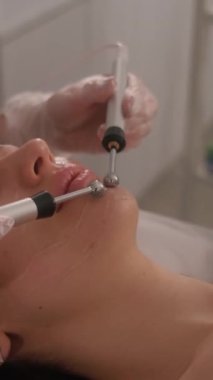 Bir güzellik uzmanının cilt bakımı prosedürleriyle yüzleşmek. Genç ve güzel bir kızın yüzünün mikro-akım terapisi. Dikey video.