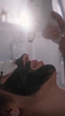 Genç ve güzel bir kızın yüzünün karbonu soyuluyor. Cilt bakımı kozmetolojisi. Lazer terapisi ve cilt tedavisi. Dikey video.