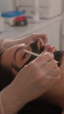Genç ve güzel bir kızın yüzünün karbonu soyuluyor. Cilt bakımı kozmetolojisi. Lazer terapisi ve cilt tedavisi. Dikey video.