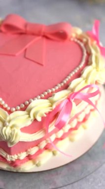 Kurdelelerle süslenmiş güzel pembe kalp şeklinde bir kekin yakın çekimi. Dikey video.