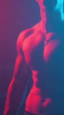 Young muscular guy in the studio with new lights and smoke. Vertical video.