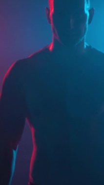 Young muscular guy in the studio with new lights and smoke. Vertical video.