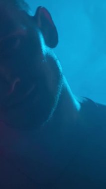 Erkek vücut geliştirici kollarındaki kasları gösteriyor. Duman içinde neon ışığı..