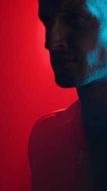 Portrait of a young pumped-up guy in the shower with fog in neon light on a black background. Vertical video.