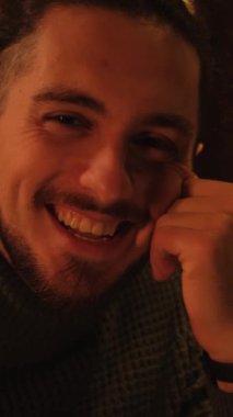 İçerideki karanlık ışıkta süveter giyen mutlu bir adamın portresi. Dikey video.