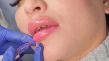 Güzellik salonunda dudaklarında kalıcı makyaj yapan genç bir kadın. Kapatın. Dikey video.