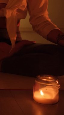 Bir kız halıya oturur ve mum ışığında yoga ve aromaterapi için tütsü yakar..