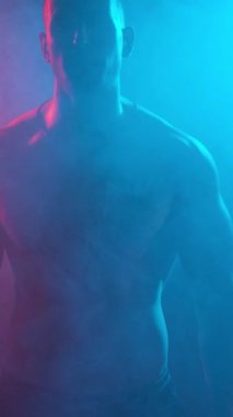 Young muscular guy in the studio with new lights and smoke. Vertical video.