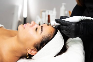 Close-up portrait of a beautiful woman with closed eyes and apparatus for skin rejuvenation. Beauty salon procedures. RF lifting. Microcurrents.