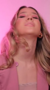 Pembe arka planda güzel makyajlı bir kızın portresi. Moda modeli. Dikey video.