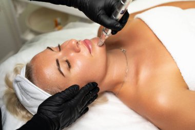 Mikroedle RF kaldırma prosedürü. Bir kozmetikçi bir kadına yüz gençleştirme ameliyatı yapar. Donanım kozmetolojisi.