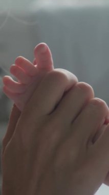 Genç anne, emziren küçük bir çocuğun bacağını öpüyor. Dikey video.