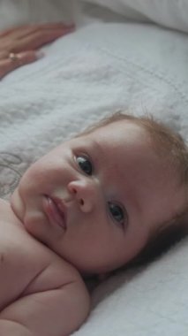 Gündüz vakti beyaz bir çarşafta çekilmiş küçük bir kızın portresi. Çocuk gülümsüyor ve merak ediyor. Dikey video.