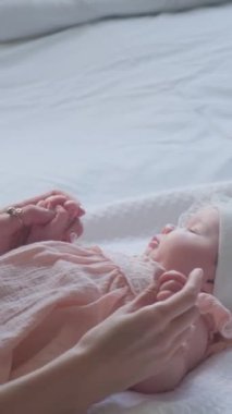 Genç anne, emziren küçük bir çocuğun bacağını öpüyor. Dikey video.