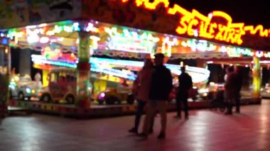 Eğlence parkındaki atlıkarıncaların renkli ışık hareketleriyle ve dönme dolabın arka planıyla gece manzarası. Bulanık video.