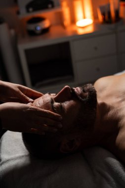 Erkek müşterisine yüz ve kafa masajı yapan profesyonel bir masözün yakın plan fotoğrafı..