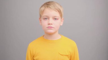 Sarı tişörtlü bir çocuk gri arka planda çığlık atıyor ve kameraya bakıyor..