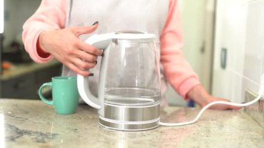 Bir kadın ısıtmak için elektrikli su ısıtıcısını açar..