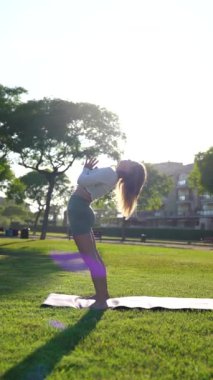 Güzel bir kız yeşil çimlerin üzerinde bir parkta yoga yapıyor. Dikey video.