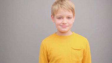 Sarı tişörtlü, gri arka planda bir çocuk göz kırpıyor ve gülümsüyor..