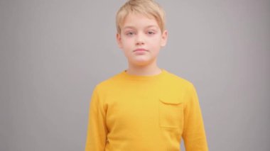 Sarı tişörtlü, gri arka planda bir çocuk göz kırpıyor ve gülümsüyor..