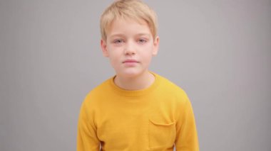 Sarı tişörtlü, gri arka planda bir çocuk göz kırpıyor ve gülümsüyor..