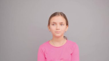 Kız düşünce ve düşünce içinde kayboldu, elini ağzına kaldırdı. Gri bir arkaplanda.