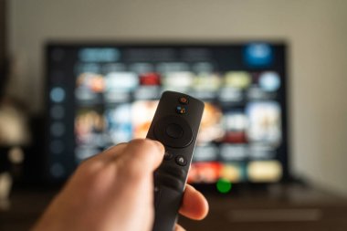 Bir kişi eli, büyük bir televizyon ekranı ile etkileşim kurmak için bir uzaktan kontrol aygıtı kullanıyor
