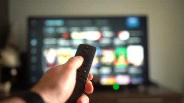 Bir kişi eli, büyük bir televizyon ekranı ile etkileşim kurmak için bir uzaktan kontrol aygıtı kullanıyor