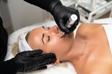 Mikroedle RF kaldırma prosedürü. Bir kozmetikçi bir kadına yüz gençleştirme ameliyatı yapar. Donanım kozmetolojisi.