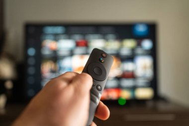 Bir kişi eli, büyük bir televizyon ekranı ile etkileşim kurmak için bir uzaktan kontrol aygıtı kullanıyor
