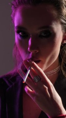 Renkli dumanlı, parlak ışıklarda güzel bir kadının moda sanat portresi. Neon ışıklı sigara içen kız. Dikey video.