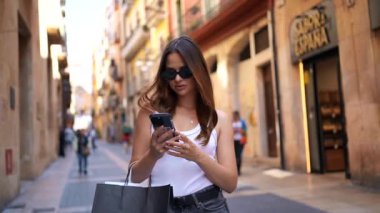 Sunny City caddesinde alışveriş yaptıktan sonra alışveriş torbaları taşıyan genç bir kadın telefonda konuşuyor..