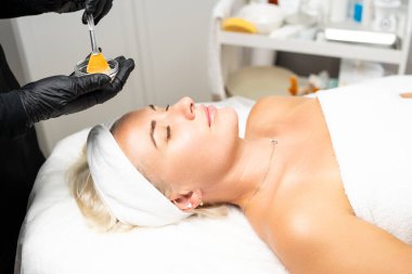 Yukarıdan gelen kozmetik uzmanı müşteriye maske takıyor, kaplıcada ya da kuaförde işlem yapıyor. Cilt bakımı, kozmetoloji ve güzellik.