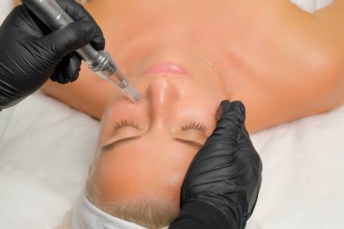 Mikroedle RF kaldırma prosedürü. Bir kozmetikçi bir kadına yüz gençleştirme ameliyatı yapar. Donanım kozmetolojisi.