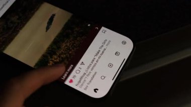 Kiev, Ukrayna - 28 Şubat 2025: Akıllı telefondaki Instagram reklamından hoşlanan bir adamın eli. Sosyal medya etkileşimi, moda içeriği, modern yaşam tarzı.