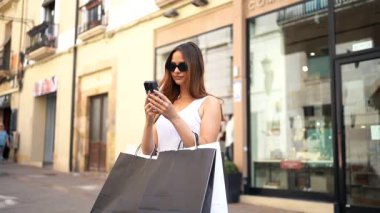 Sunny City caddesinde alışveriş yaptıktan sonra alışveriş torbaları taşıyan genç bir kadın telefonda konuşuyor..