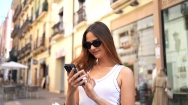 Sunny City caddesinde alışveriş yaptıktan sonra alışveriş torbaları taşıyan genç bir kadın telefonda konuşuyor..