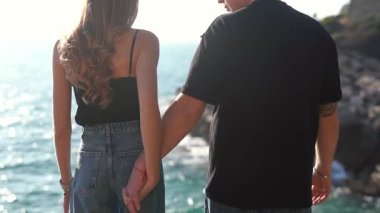 Deniz kenarında el ele tutuşan bir çiftin yakın çekimi aşkı, bağlantıyı ve birlikteliği sembolize ediyor..