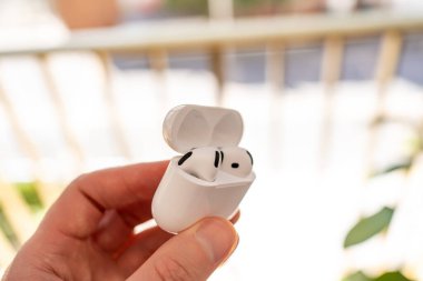 Bir adam açık beyaz şarj çantasında bir çift kablosuz kulaklık tutuyor..