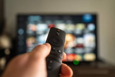 Bir kişi eli, büyük bir televizyon ekranı ile etkileşim kurmak için bir uzaktan kontrol aygıtı kullanıyor