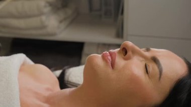 Estetisyen, kozmetik enjeksiyonundan önce bir kadının dudaklarına pamuk çubukla krem sürer. Kadın bir güzellik kliniğinde tedavi yatağında yatıyor..