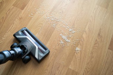 Elektrikli süpürge hortumu dağınık pirinç tanelerini ahşap zemin temizleme, dağınıklık ve ev bakımı konseptinden topluyor..